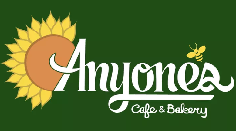 Anyone's Cafe & Bakery logo: a yellow sunflower against the A in Anyone's and a bee in the palce of an apostrophe between the e and s in white script against a dark green background